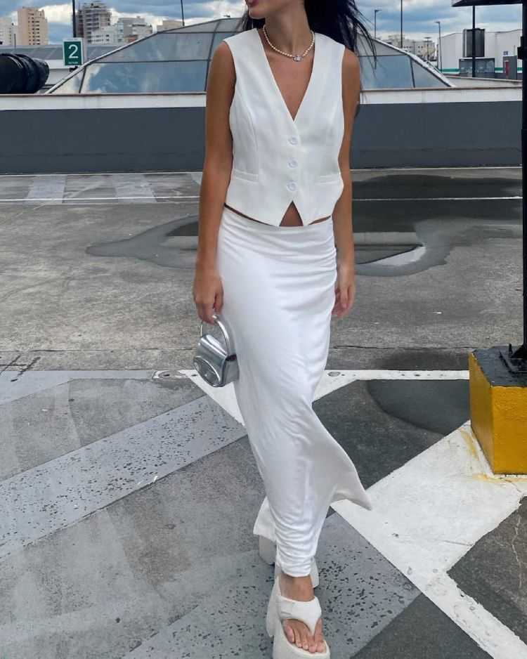 Natalia Cangueiro com colete de alfaiataria branco, saia longa branca, sandália de plataforma branca e bolsa pequena prateada