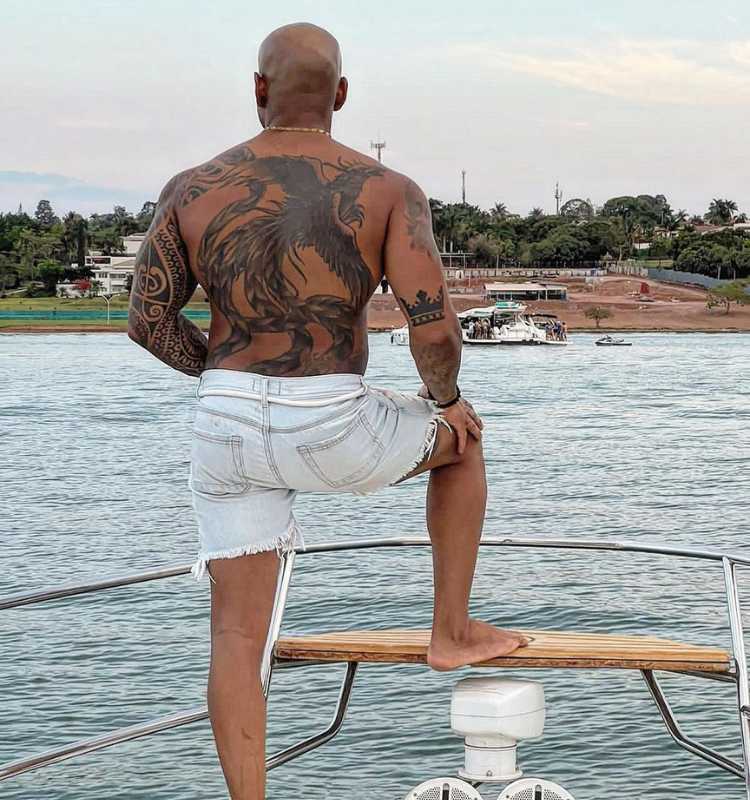 Cezar Black do BBB 23 de costas sem camisa em embarcação no mar. Na foto é possível ver suas tatuagens.