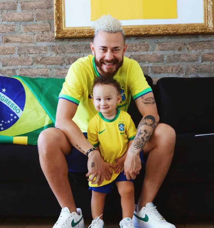 Fred do BBB 23 com seu filho que teve Bianca Andrade, influenciadora, sentados no sofá com bandeira do Brasil. Na foto, é possível ver as tatuagens do brother.