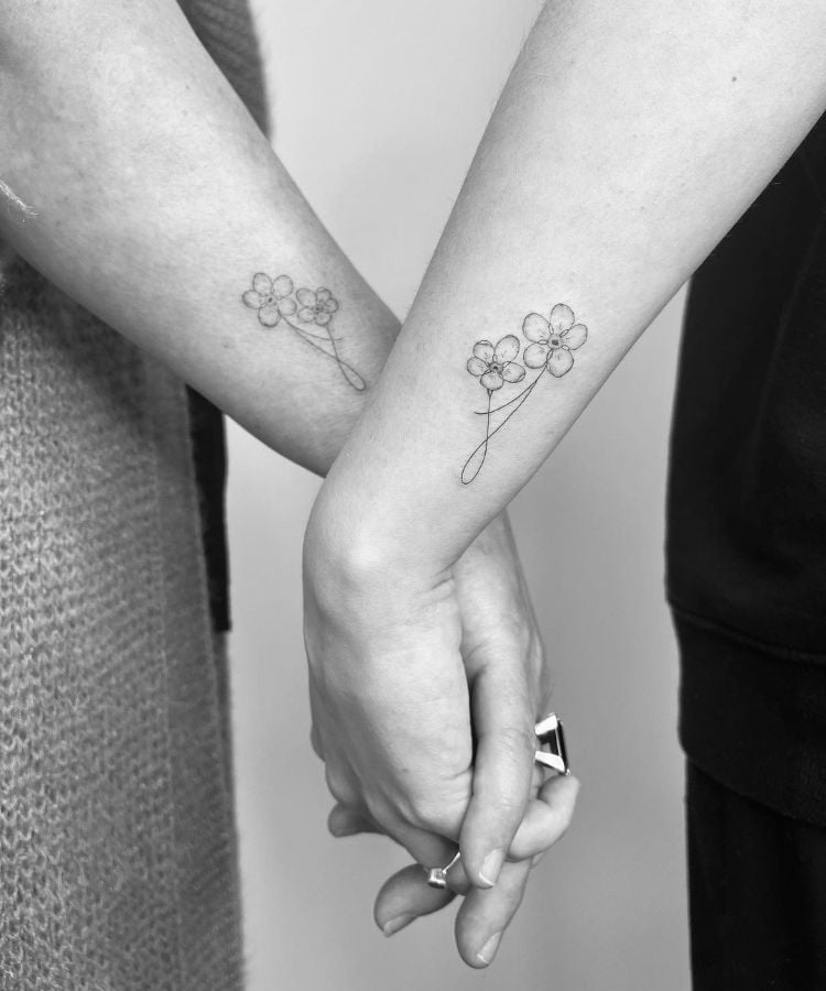 mãe e filha de mãos dadas com tatuagem de flores na lateral do braço