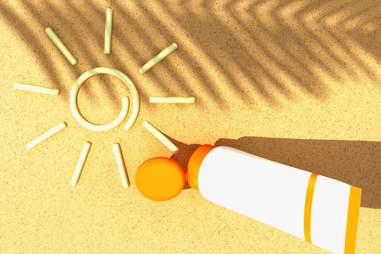 foto de protetor solar com cor fazendo desenho de sol na areia