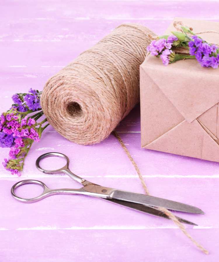 Barbante, tesoura, caixa e flores sob superfície cor-de-rosa.