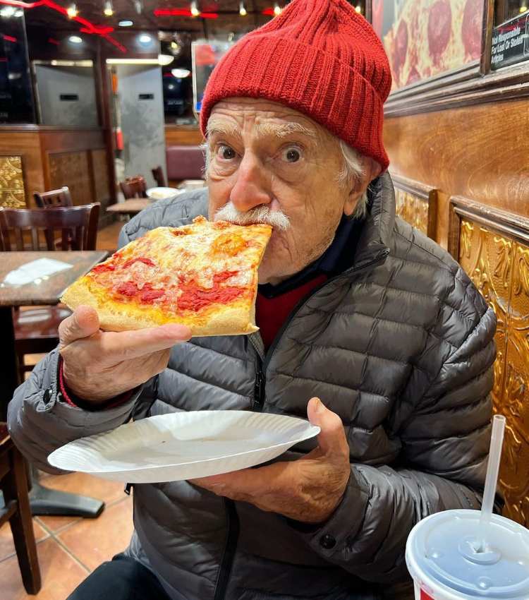 Ator Ary comendo pizza com a mão em pizzaria.