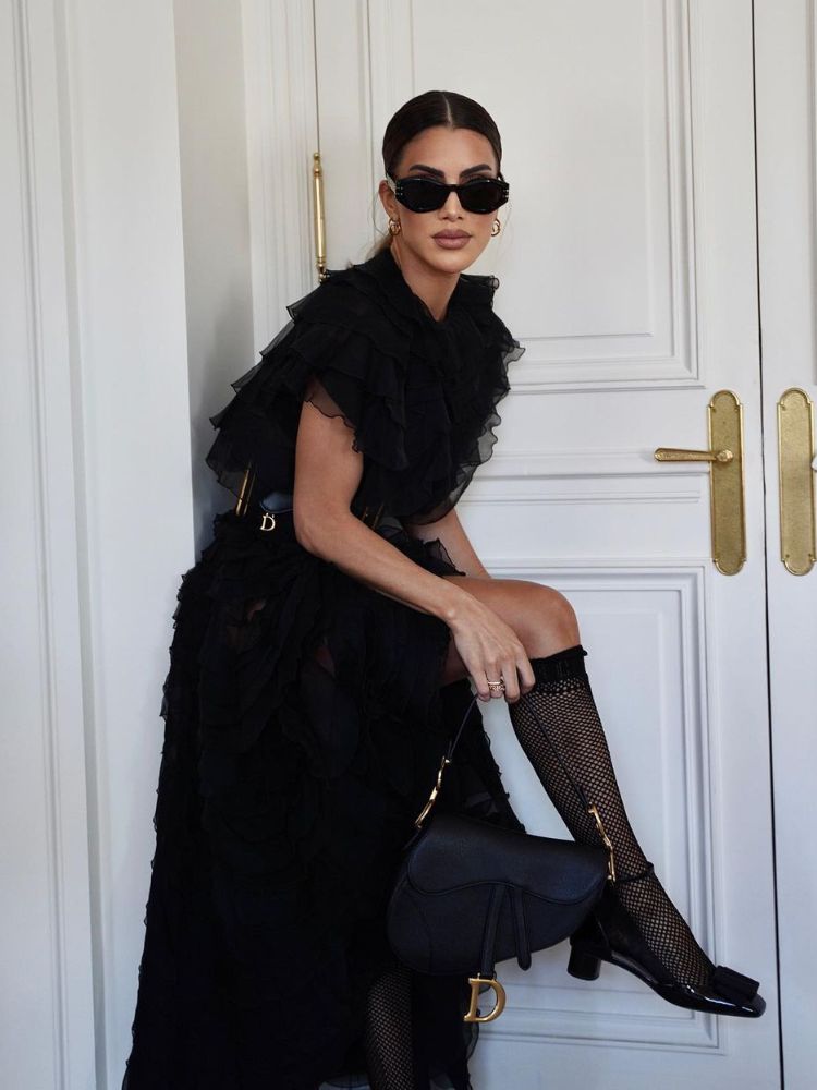 foto de influencer camila coelho na paris fashion week, com vestido preto com babados, acessórios pretos, sapato e meia. 