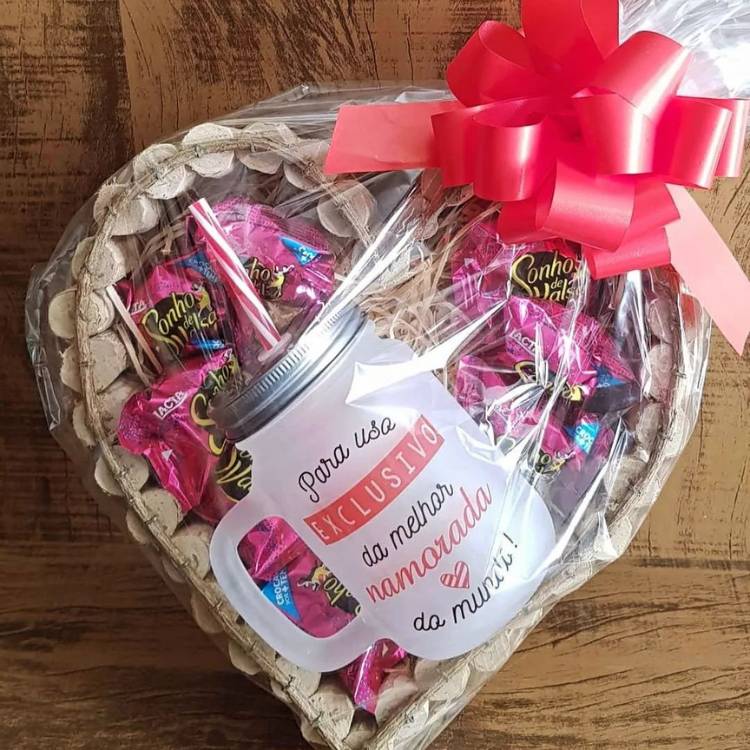 Cesta de Páscoa em formato de coração com vários bombons sonho de valsa e uma caneca para a namorada, dentro de saco transparente com laço.