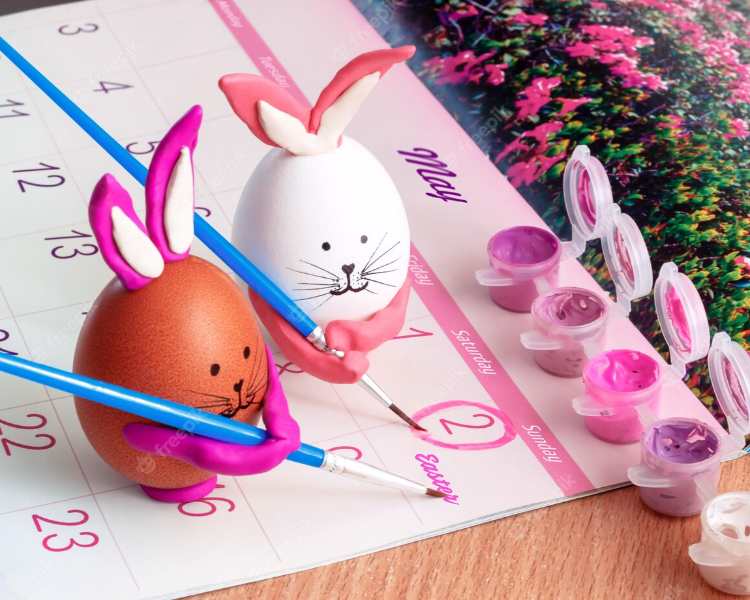 Dois ovos de galinha com rostinho e orelhas de coelho segurando pincel marcando data da Páscoa em calendário.