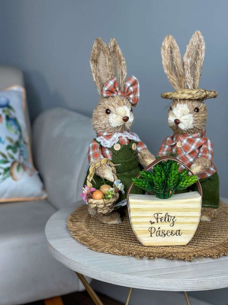 Casal de coelhos de tecido enfeitando mesinha na sala com um vasinho de madeira escrito "Feliz Páscoa"