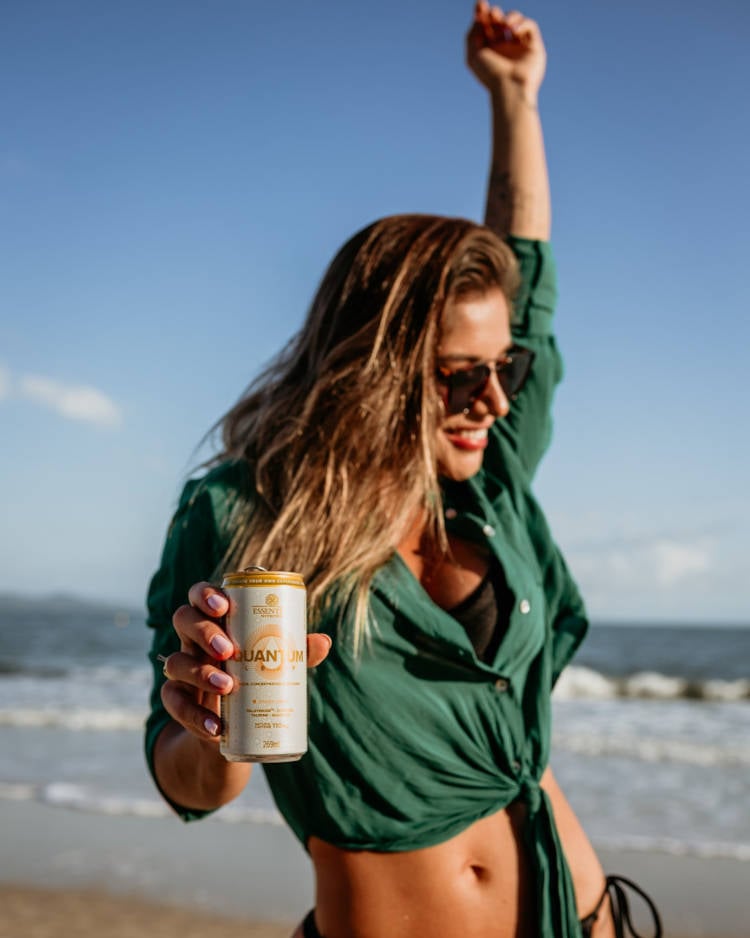 Mulher na praia com lata de bebida saudável e refrescante.