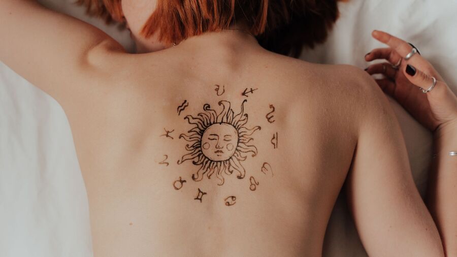 mulher deitada de costas com uma tatuagem de horóscopo nessa área