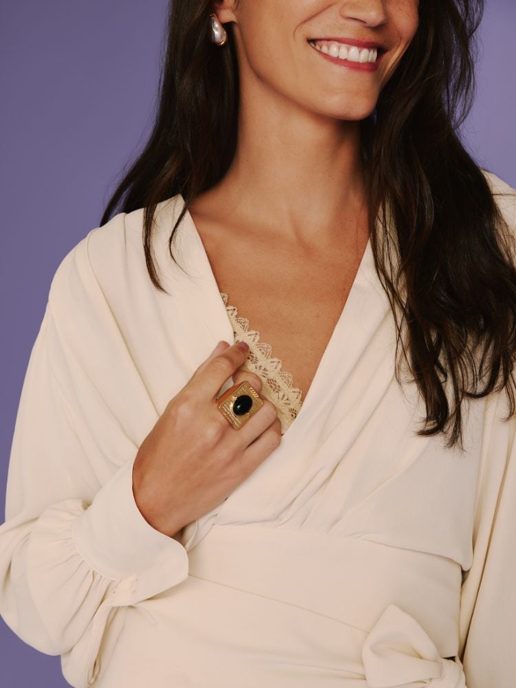 foto em close no colo da modelo, mostrando anel dourado com pedra preta e brinco com pedra branca
