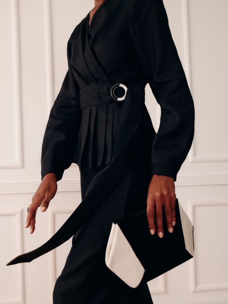 modelo utilizando calça e casaco de linho, pretos, e bolsa com recorte geométrico preto e branco. 