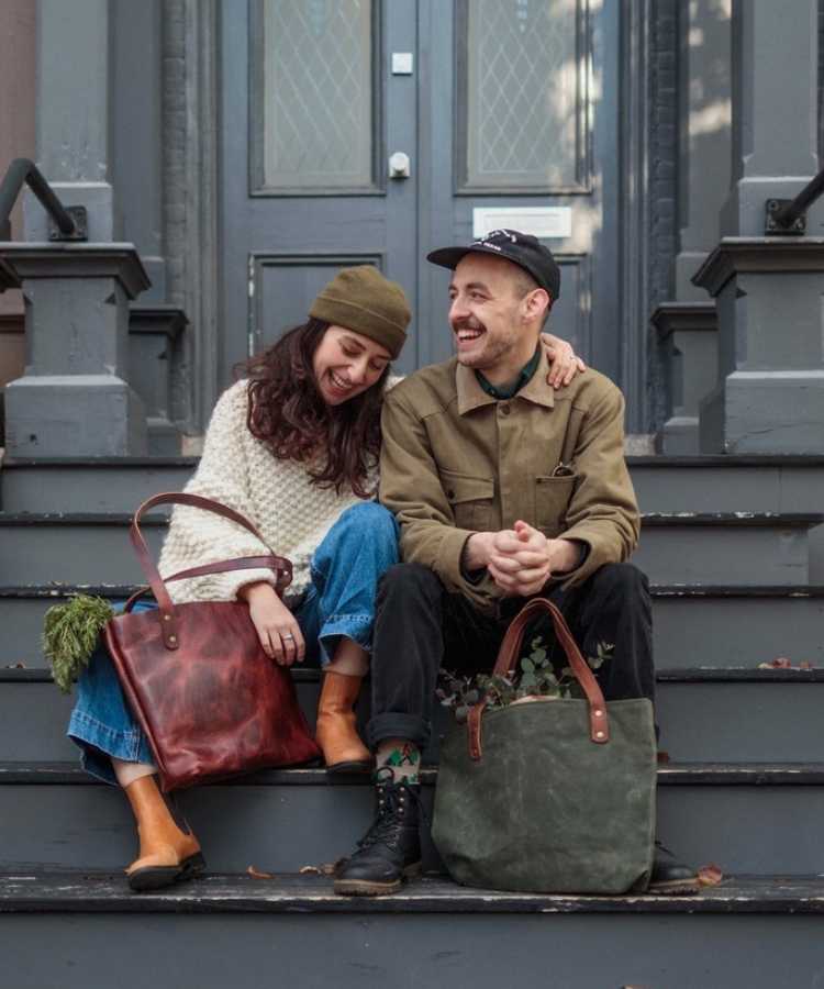 Mulher e homem sentados em escada de casa com looks tendência: : bolsas tote.