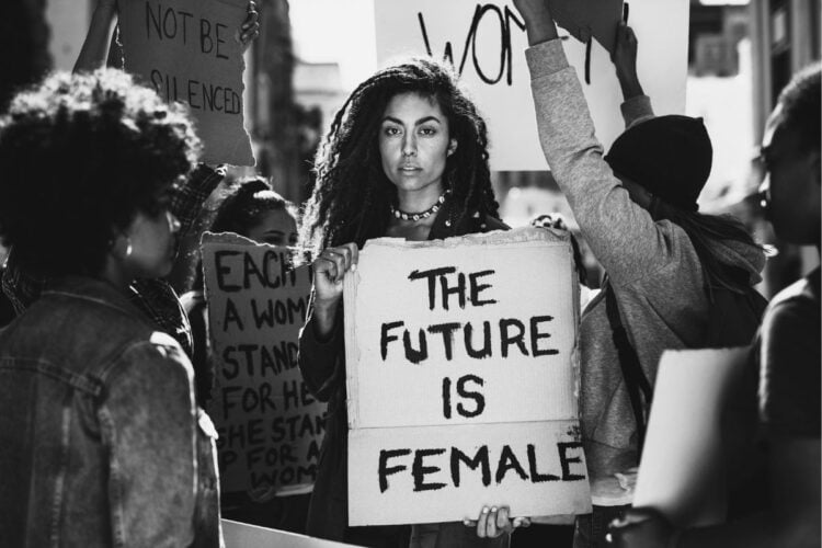 Mulher em protesto com outras mulheres, segurando placa escrito O futuro é feminoin em inglês