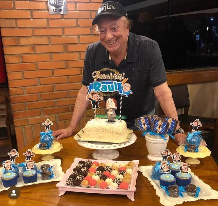 Apresentador de frente a mesa com doces e bolo para seu aniversário em 2023.