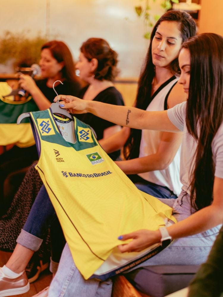 na imagem, jogadora Natinha segura camisa amarela do uniforme do vôlei de quadra feminino. 