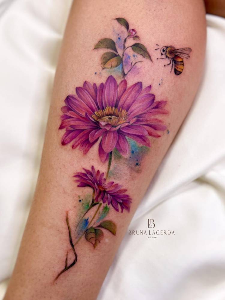 Tatuagem de gérbera colorida em roxo, azul e verde, com abelha colorida. 