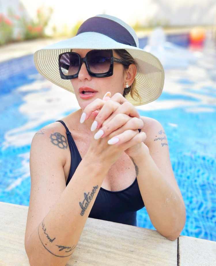 Antonia Fontenelle na piscina com maio preto, óculos escuro e chapéu