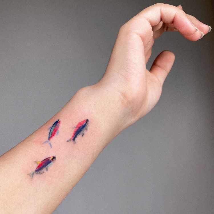 3 peixes azul e vermelho tatuados na lateral do pulso