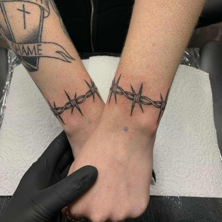 dois pulsos tatuados com bracelete arame farpado