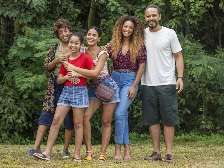 Personagens da família de Sol da novela Vai na Fé da Globo, reunidos em frente a local com vegetação.