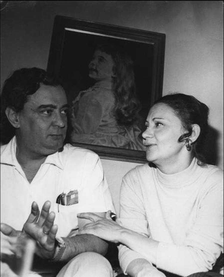 A atriz e seu falecido esposo, Fernando Balleroni, sentados em fundo de parede com quadro de menina.