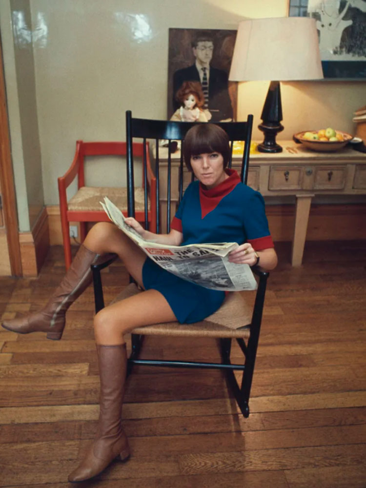 Mary Quant lendo jornal sentada usando conjunto com minissaia