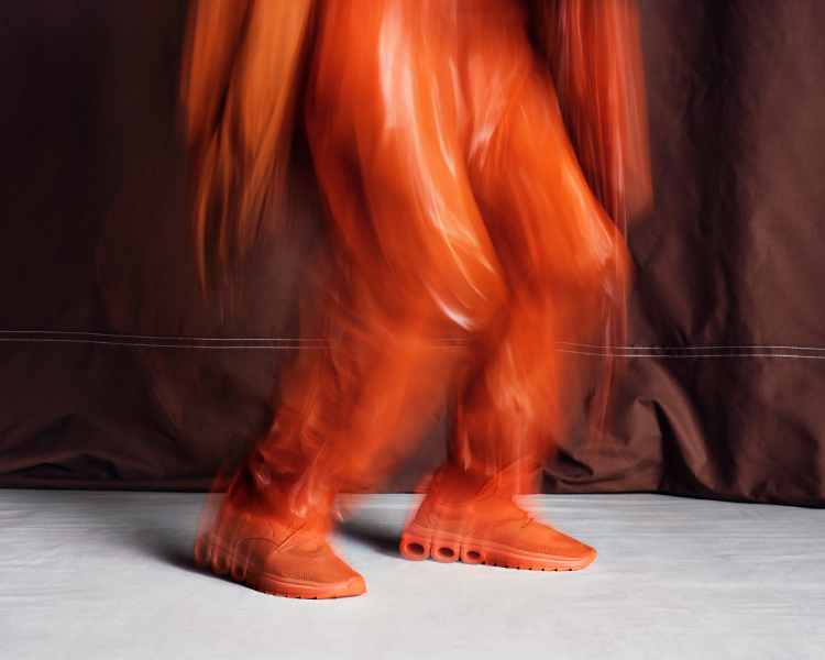 Foto de de ensaio do do novo tênis Ferragamo. Modelo em movimento com roupa de mesma cor que o calçado laranja
