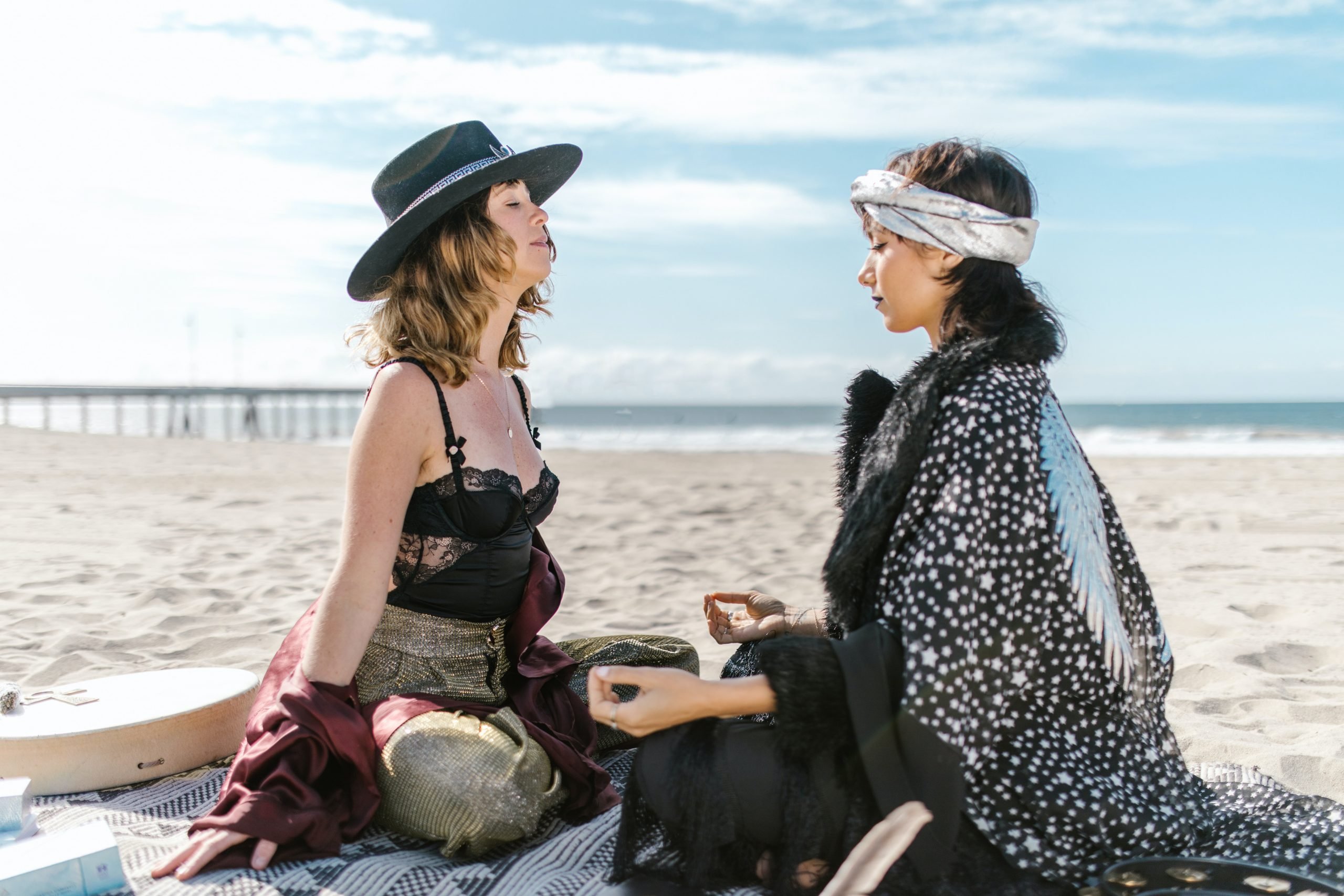 duas mulheres na praia, com roupas largas e em posição de meditação