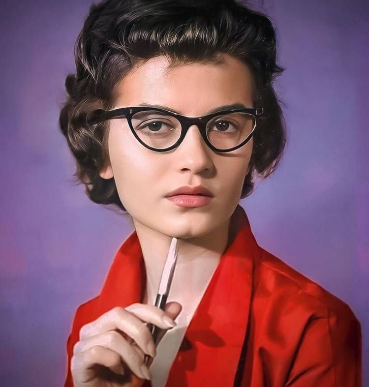 Rosamaria em foto antiga, de óculos e segurando caneta.
