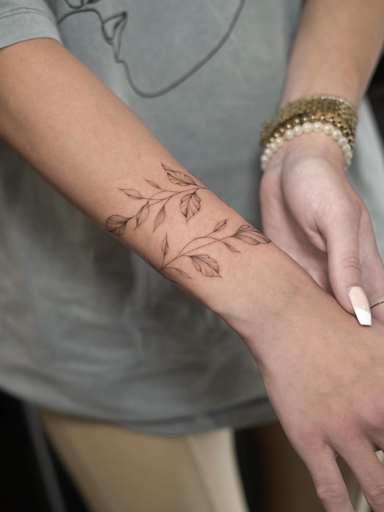 Pessoa de pele clara com blusa cinza e tatuagem de ramo no pulso formando bracelete
