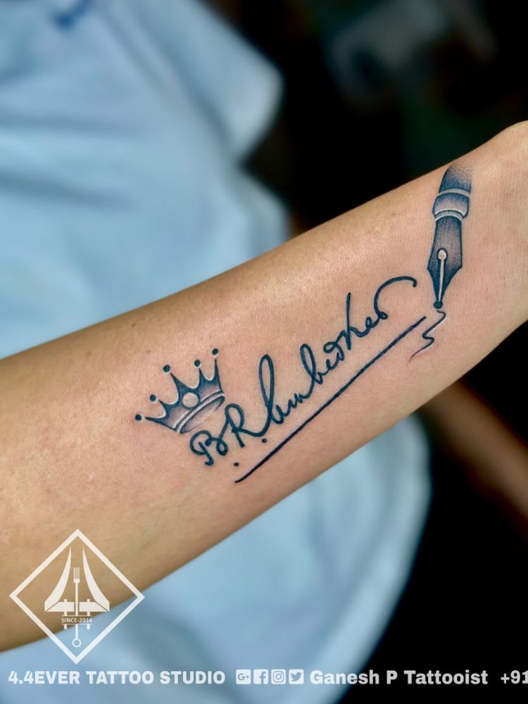 Pulso tatuado com assinatura, coroa e caneta-tinteiro
