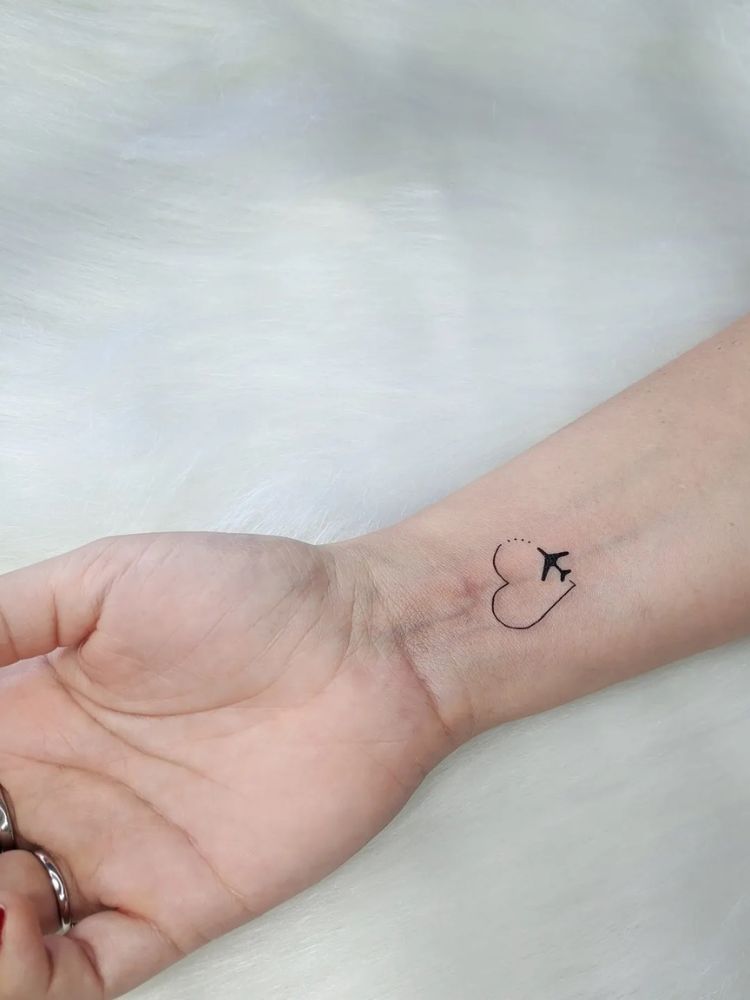 Pulso interno de pessoa de ele clara com tatuagem de coração pontilhado e avião