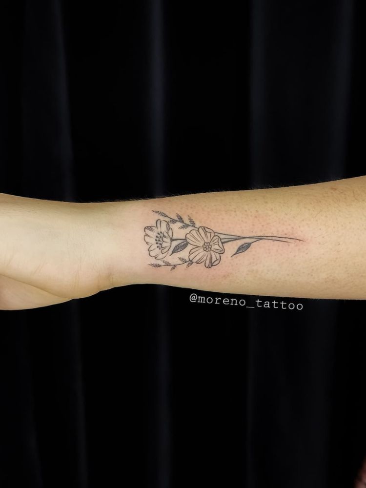 Braço de pessoa de pele clara com duas flores tatuadas em fine line