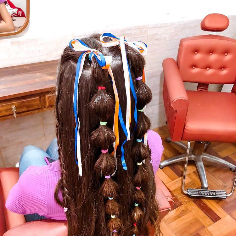 bubble braids em cabelo castanho escuro decoradas com fitas e elásticos coloridos.