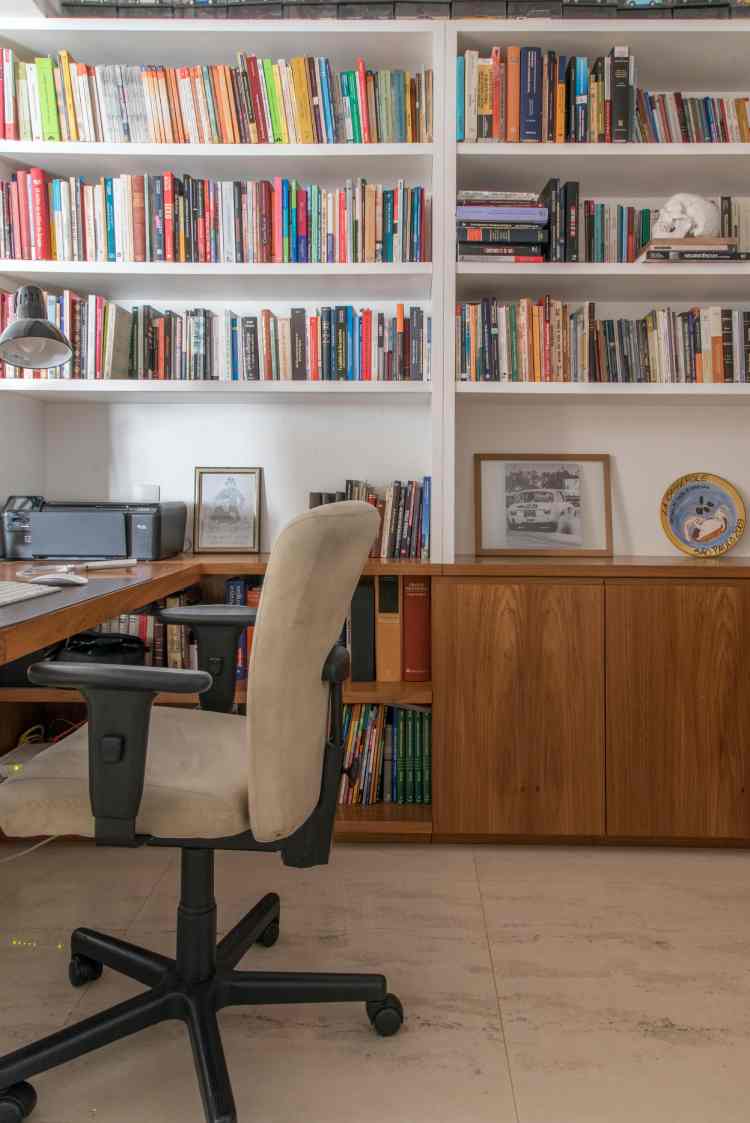 cantinho de leitura com parede de estante de livros e escrivaninha branca ao lado