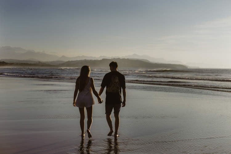 Casal jovem andando de mãos dadas na praia