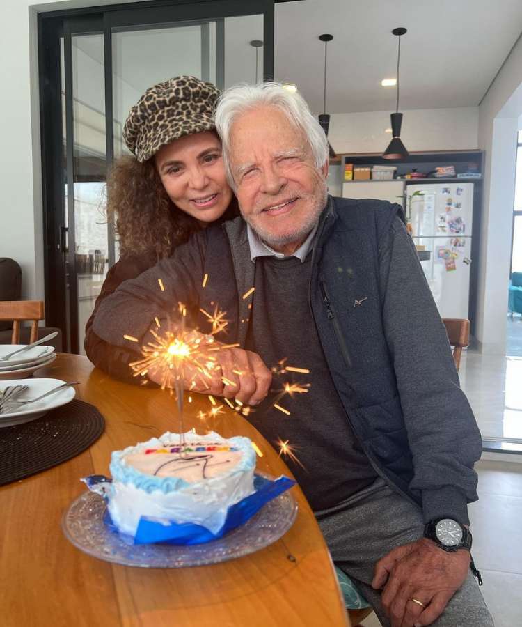Fátima Sampaio e o marido Cid Moreira sentados em mesa com bolo de aniversário 