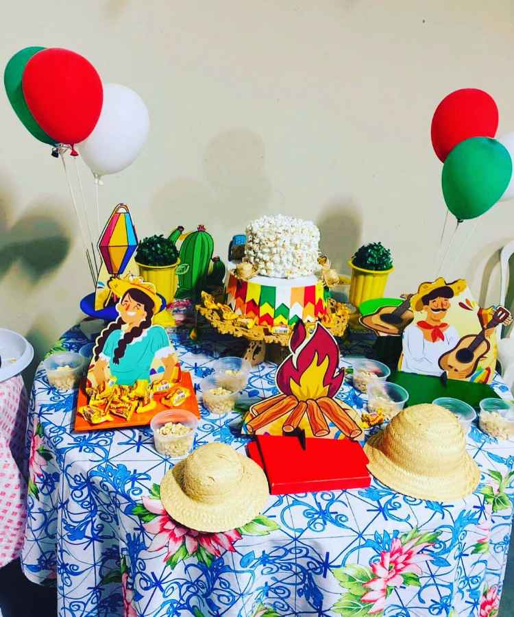 Decoração em mesa de festa junina simples, contendo doces, bolos, paçoquinhas, com enfeites de papel