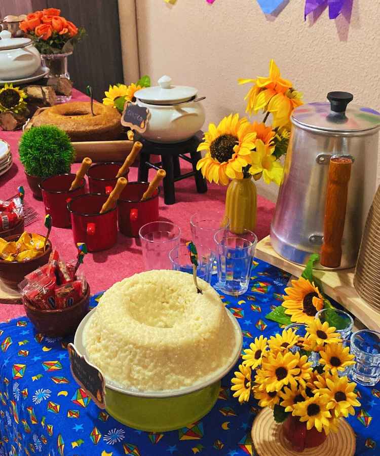 Decoração em mesa de festa junina simples, contendo doces, bolos, canecas, copos, enfeites, etc