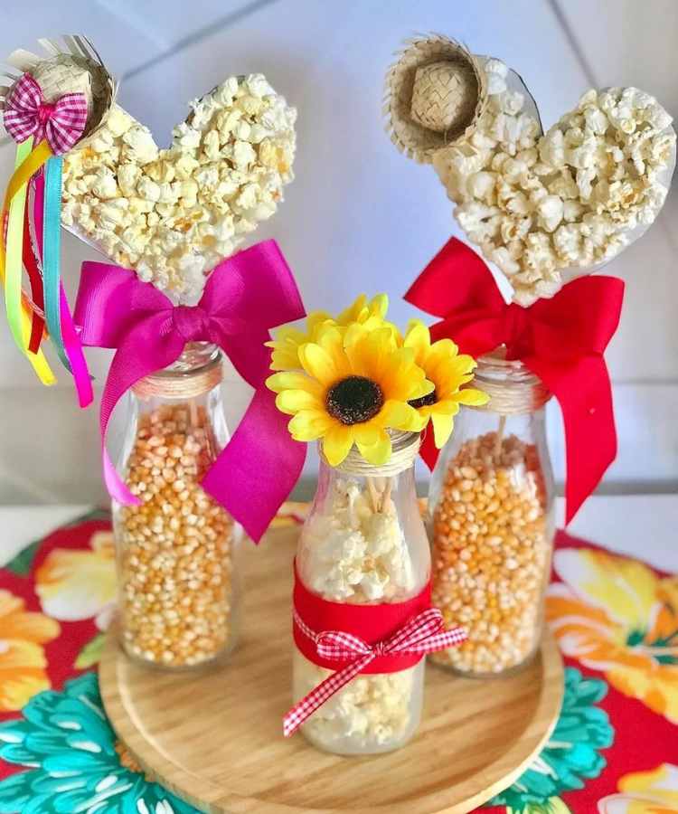 garrafas de vidro com milho de pipoca cru e frito, decorado com laços, com flores de girassol, e coração de pipoca, além de minis chapéus de palha