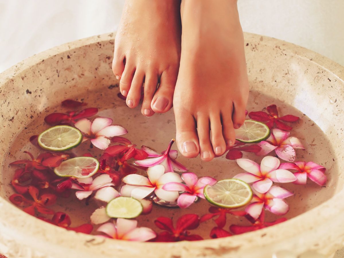 Escalda-pés: foto de pés entrando em bacia com água quente, flores, bruvas, ervas e essencia.
