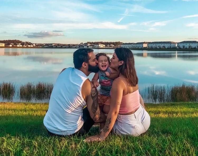 Lucas Lira, Noah e Sunaika Bruna sentados em frente a lago em Orlando, nos EUA