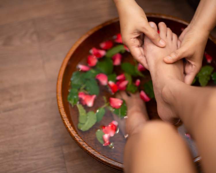 Escalda pés com ervas frescas e pétalas de flores, mãos fazendo massagem nos pés