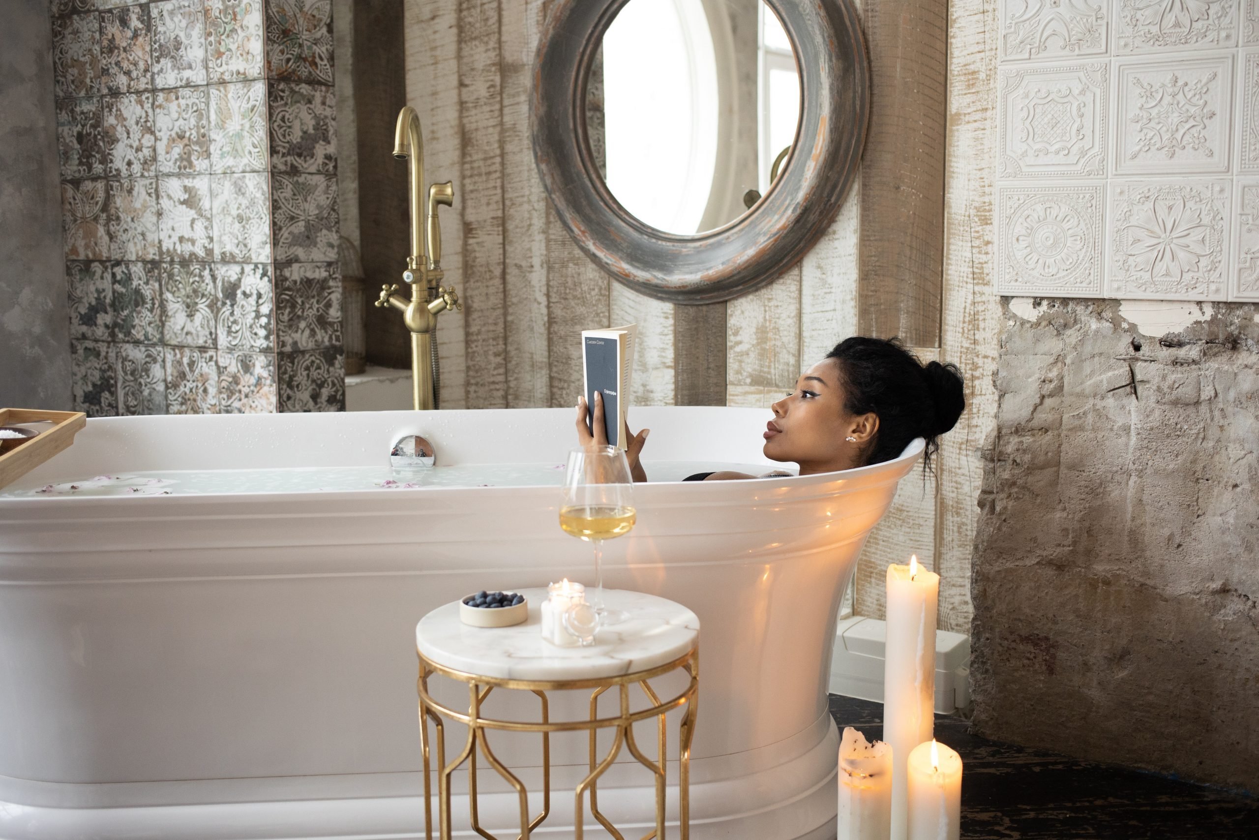 mulher na banheira para um ritual de relaxamento com velas e lendo um livro