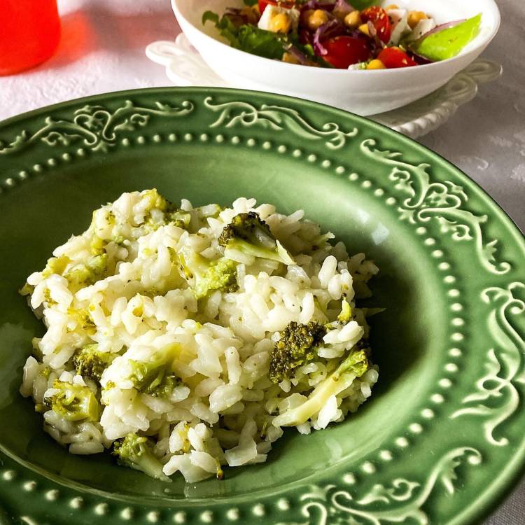 Prato verde fundo com risoto de brócolis, sobre mesa e com tigela branca de salada ao lado