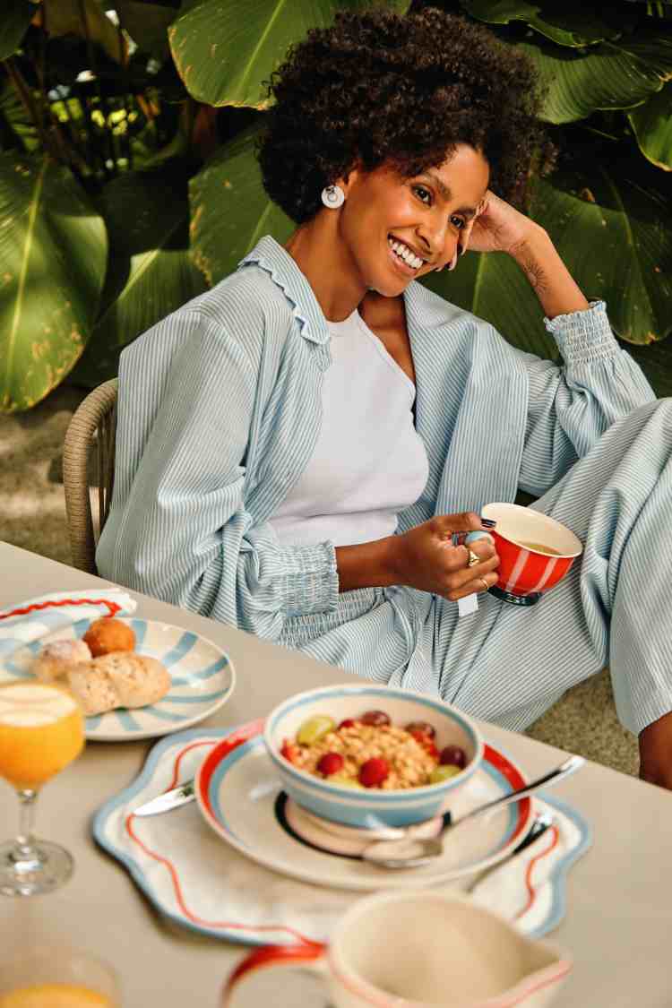 mulher com conjunto de camisa e calça azul claro segurando xícara enquanto está sentada