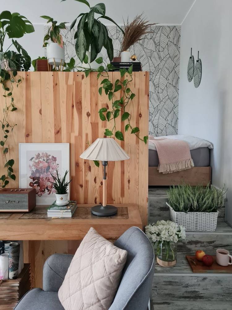 Foto de divisão de ambientes por bandô de madeira, decorado com plantas, além de mesa com cadeira, quadros, abajur e vaso 