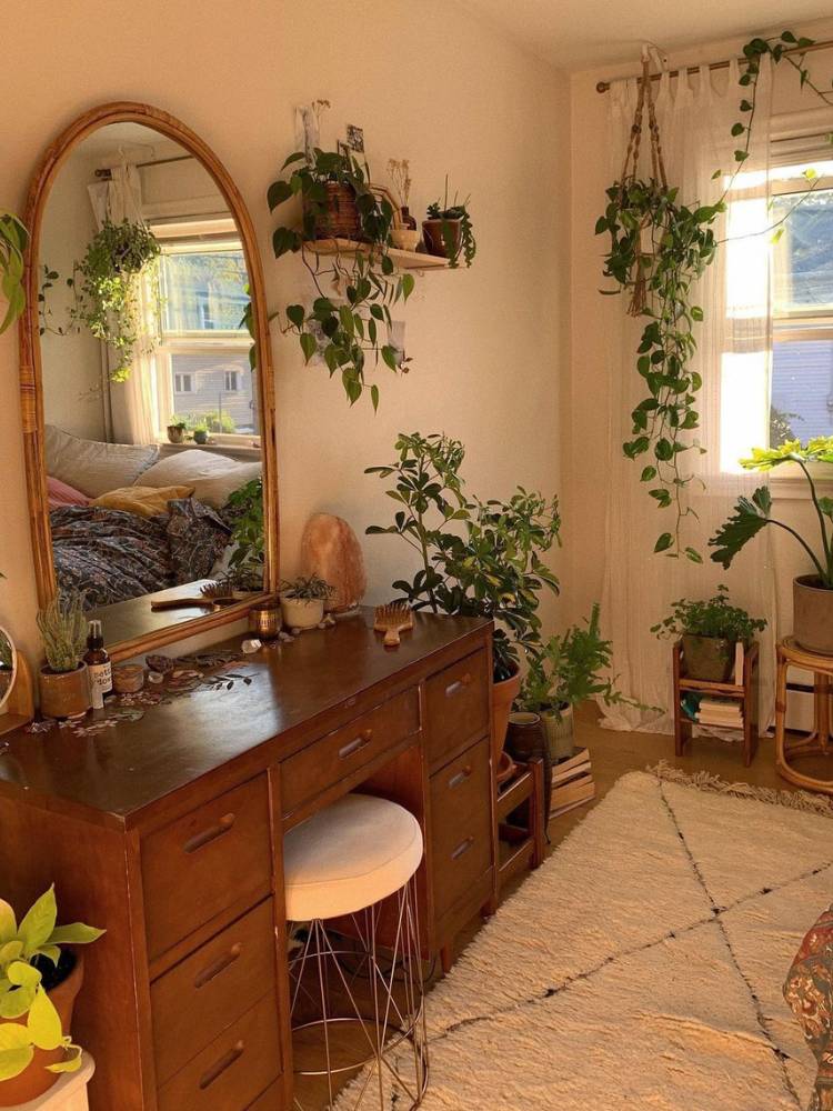 Canto de quarto com penteadeira de madeira, banco, espelho grande e plantas pendentes e em vasos 