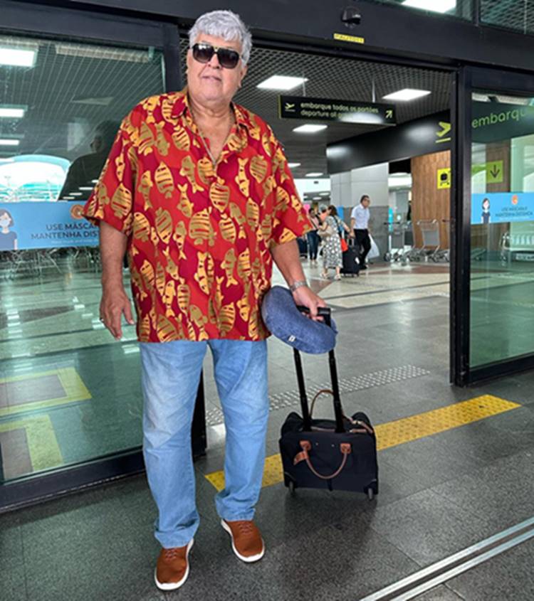 Sidney Magal em aeroporto com mala e almofada de pescoço para viajar
