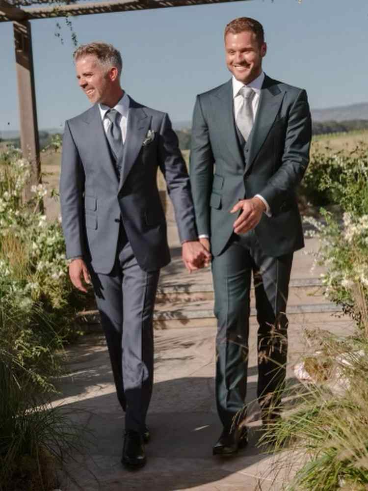 Noivos Colton Underwood e Jordan C. Brown se casando. Eles usam ternos cinza e verde-escuro.
